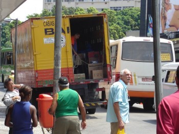 De um lado caminhões estacionados; de outro, carros e motos. No meio, automóveis esperam para pass